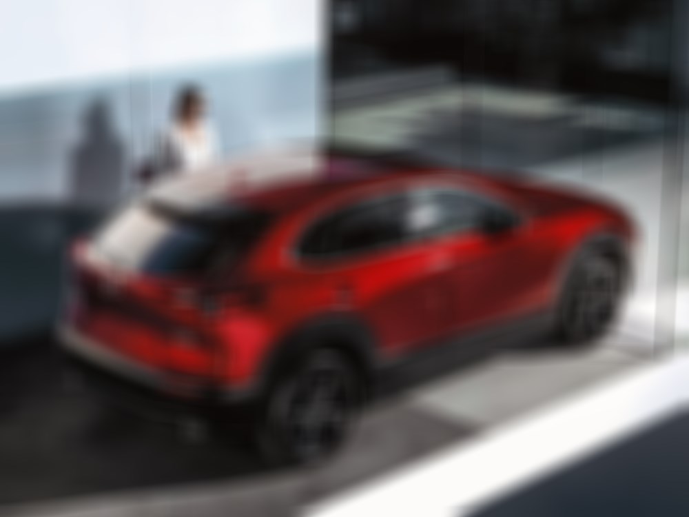 Une professionnelle portant des lunettes de soleil s’approche d’un Mazda CX-30 rouge vibrant cristal métallisé dans une entrée. 