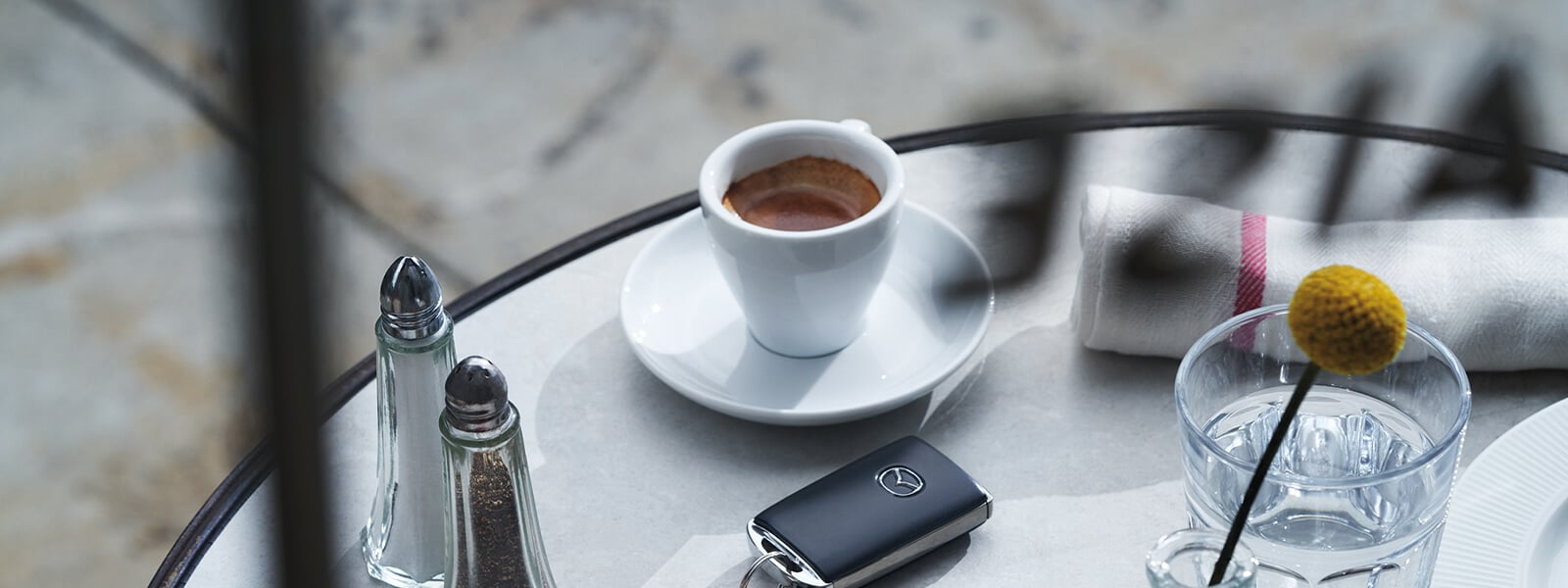 Vue de dessus d’une table avec des salières et poivrières, une pâtisserie, une tasse de café et un porte-clé Mazda.