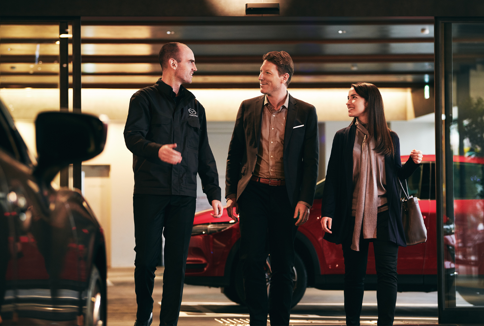 Un technicien du service Mazda discutant avec un homme et une femme s’éloignant d’une Mazda rouge située dans l’aire de service derrière eux 