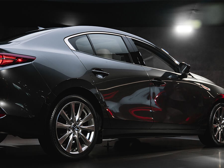 Gleaming black Mazda3 sedan seen from passenger-side taillight.