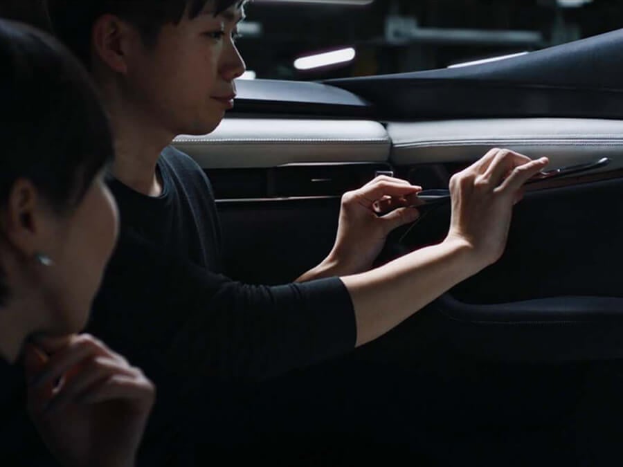 Les mains d’un technicien Mazda captent la lumière alors qu’il ajuste l’intérieur d’une voiture sous le regard d’une collègue.