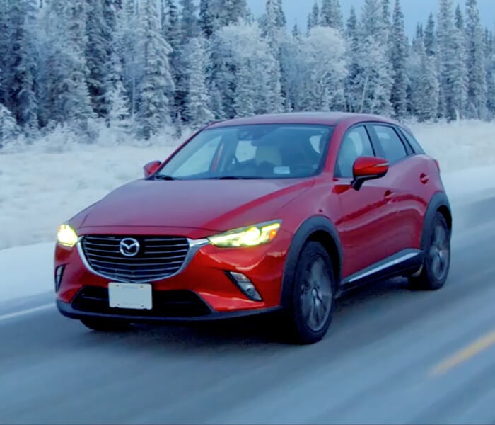 Red Mazda SUV drives on highway past stand of snow-covered trees