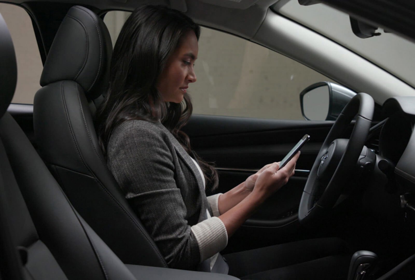 Le conducteur d’une Mazda garée regarde son téléphone intelligent. 
