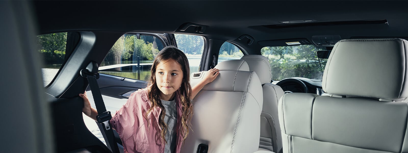 Fille en veste rose regardant à travers la porte du passager arrière côté conducteur, dans le compartiment arrière d’un VUS Mazda