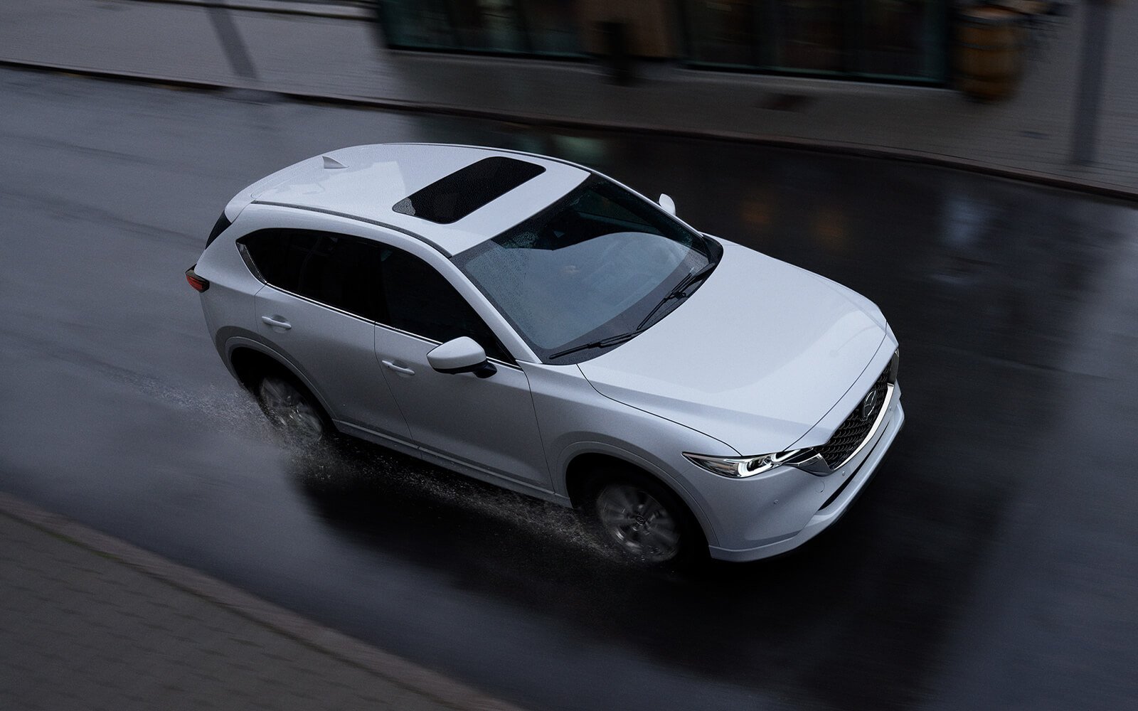 Mazda MX-30 blanc avec toit ouvrant fermé descendant une rue sous la pluie