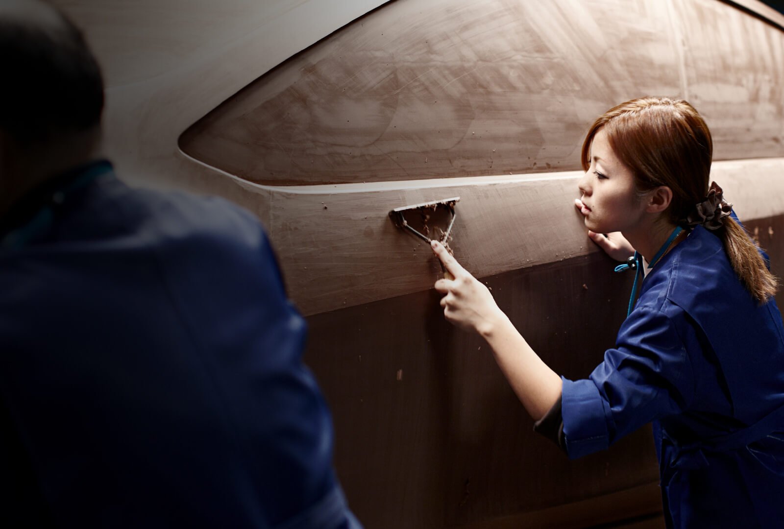 A female Takumi uses scraping tool to shape a clay Mazda form