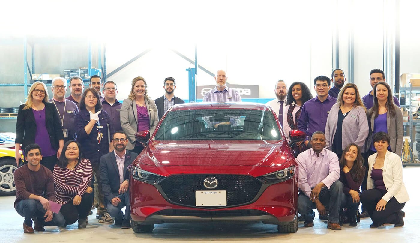 Photo de groupe du personnel d’un détaillant Mazda se tenant debout ou agenouillé, de chaque côté d’une Mazda3 rouge.