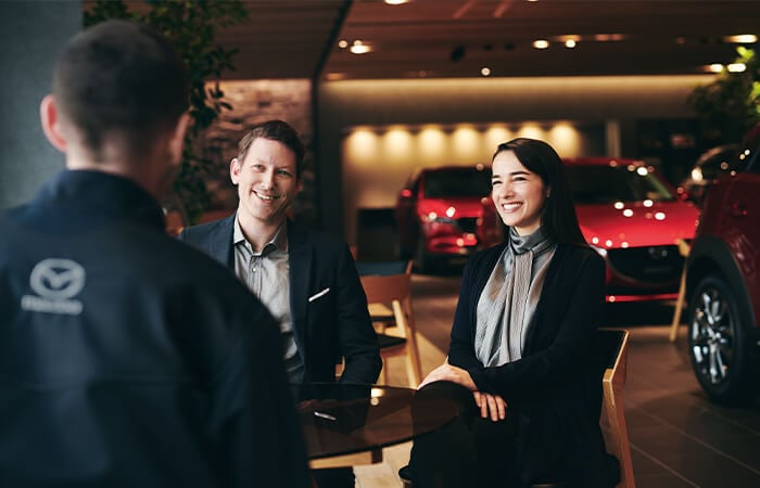 Professional couple smile as they listen to a Mazda service technician.