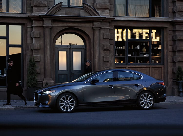 Un piéton jette un second regard, alors qu’il passe à côté d’une berline Mazda stationnée en ville, devant un vieil hôtel