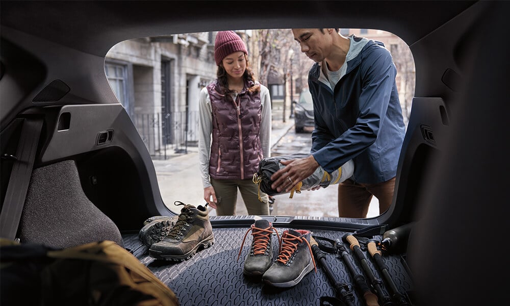 Young couple dressed for the outdoors placing items for a camping trip into the liftgate of a Mazda SUV