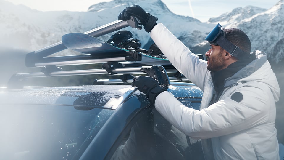 Un homme debout à côté d’une Mazda3 avec un porte-planche à neige monté sur le toit