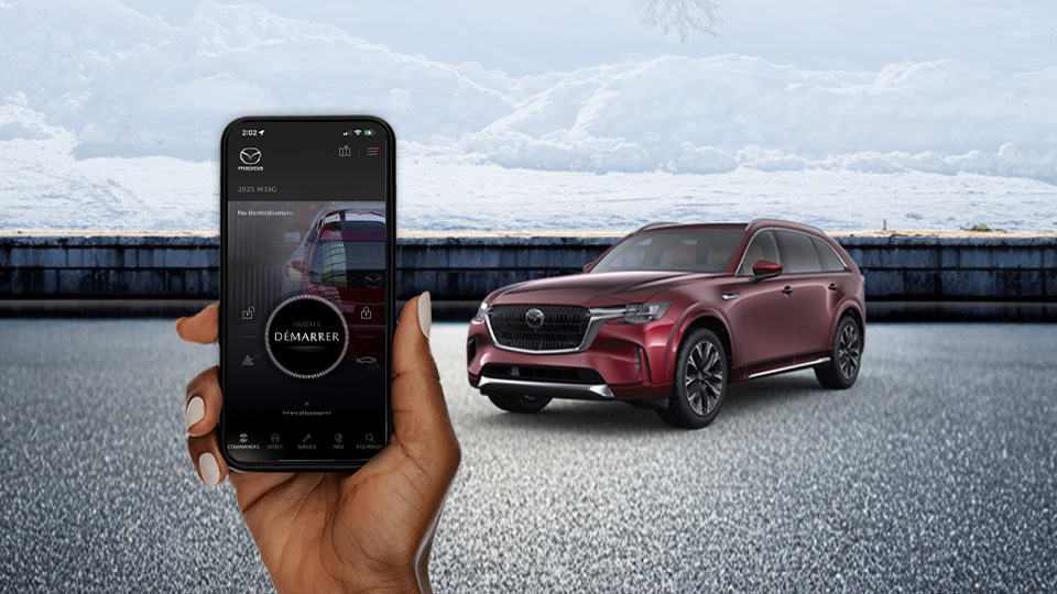Une main tenant un téléphone sur lequel l'appli MyMazda est ouverte; un CX-90 est présent en arrière-plan