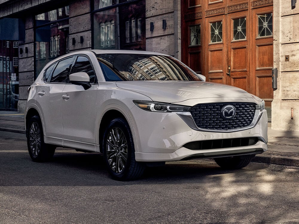 Snowflake White Pearl Mazda CX-5 parked alongside urban retail stores at twilight