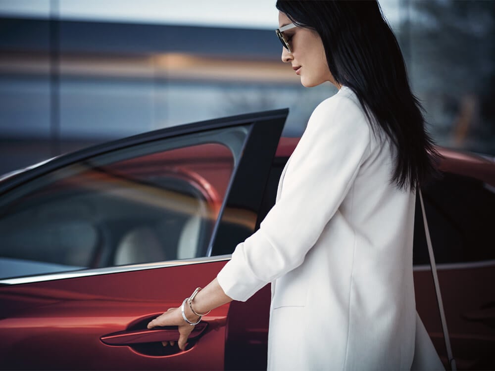 Woman in white blazer and sunglasses opens driver-side door of red Mazda.