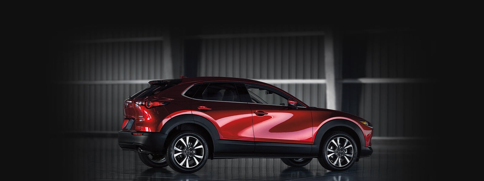 Soul red crystal Mazda SUV gleaming in passenger side profile against a dark background