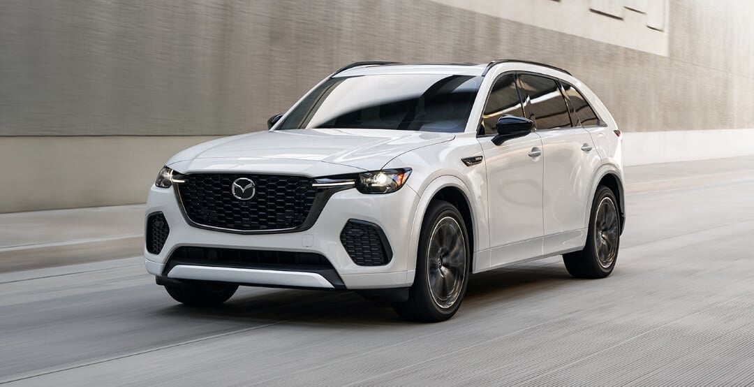 Vue trois quarts avant du Mazda CX-70 hybride léger blanc rhodium métallisé roulant sur une autoroute en béton.