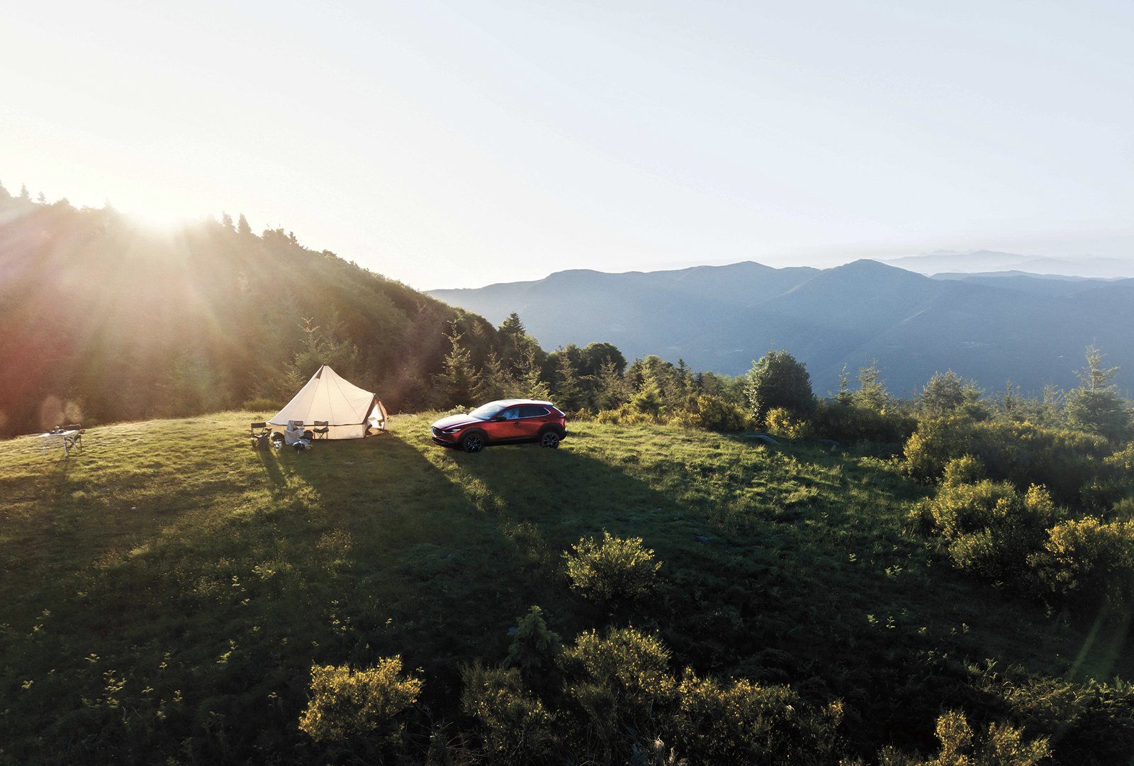 Un Mazda CX-5 stationné près d’une grande tente plantée sur une verdoyante butte, avec d’autres collines à l’horizon.
