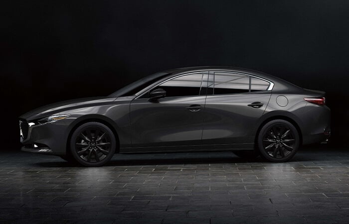 Profil du côté conducteur de la Mazda3 noir de jais mica reflétant la lumière dans un studio.