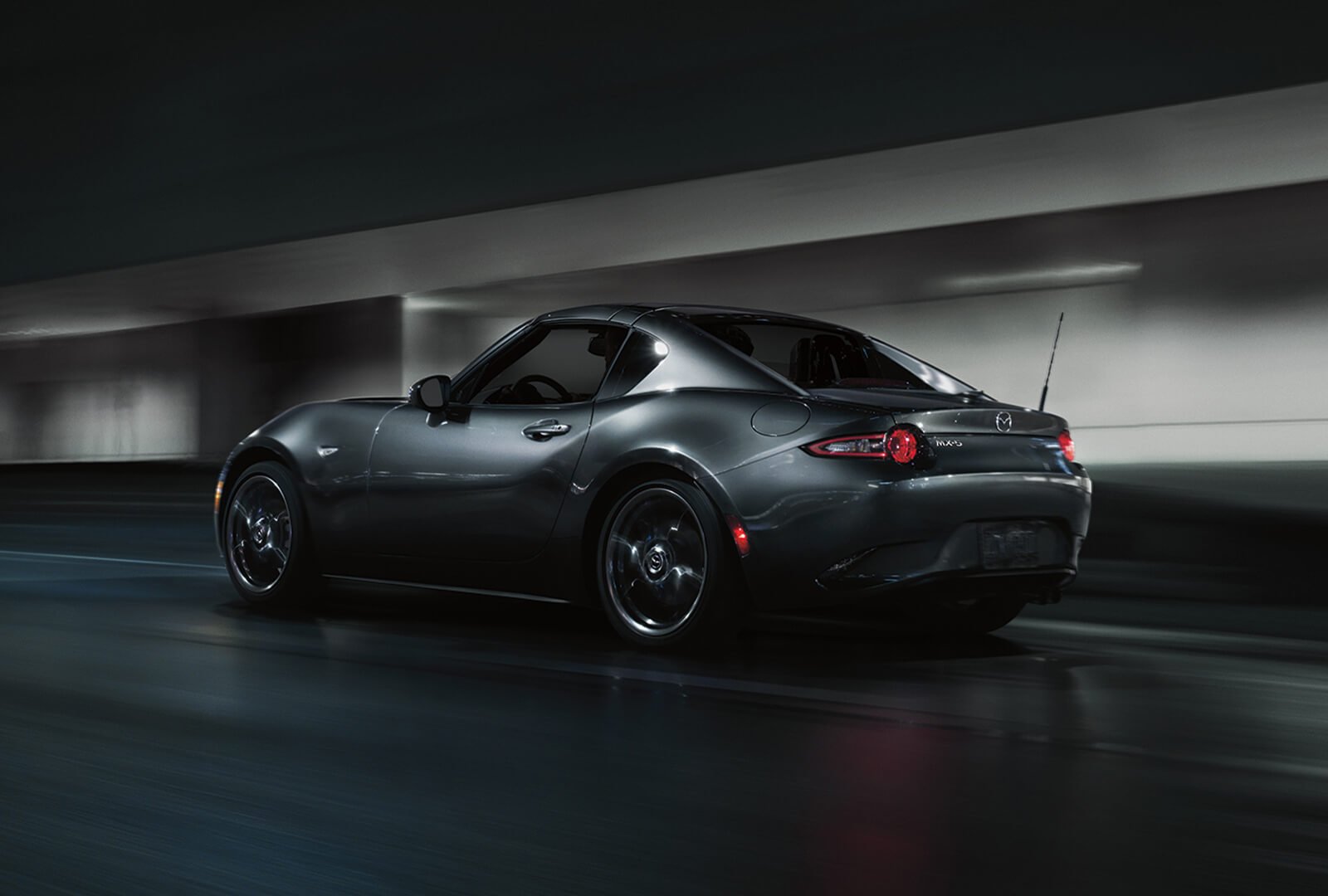 Gleaming Polymetal Grey Metallic Mazda MX-5 RF with roof up pulls away past blurred tunnel walls.