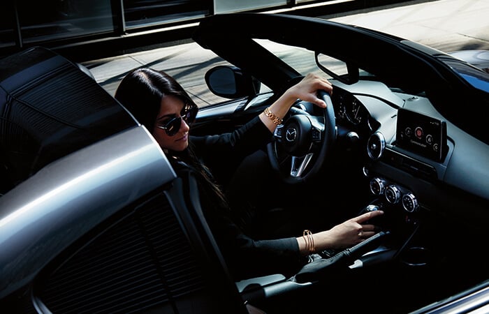 A woman in sunglasses interacts with the centre console inside the MX-5.