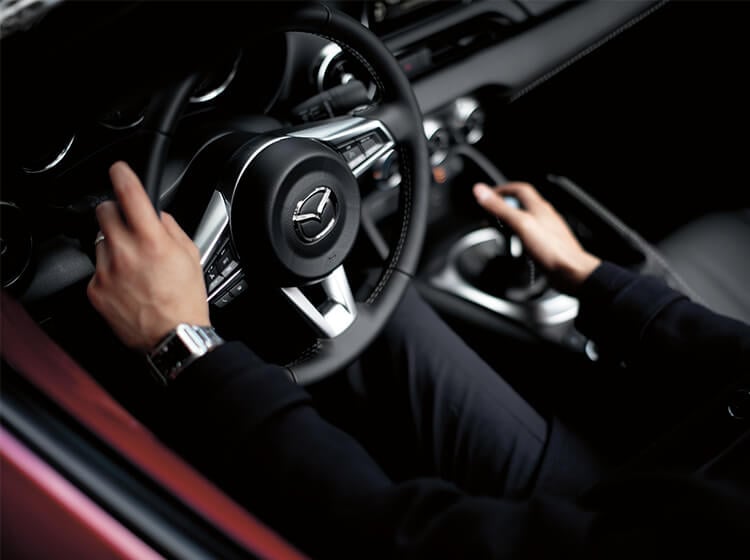 Over-shoulder view of driver holding steering wheel with left hand and grasping shifter with right