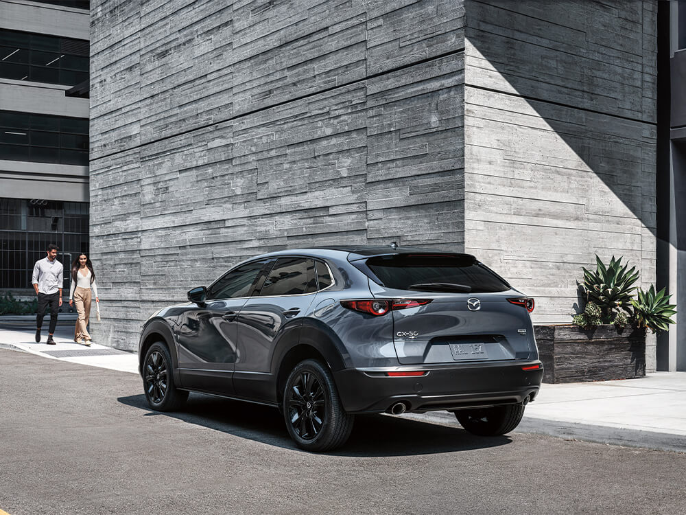 Couple approach Machine Grey Metallic Mazda CX-30 parked in front of a hotel.