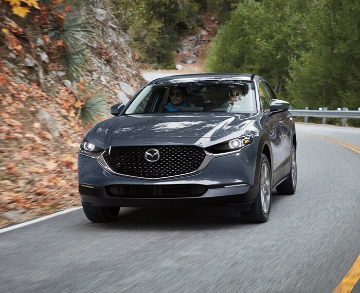 Machine Grey Metallic Mazda CX-30 takes a slight turn on an escarpment road.