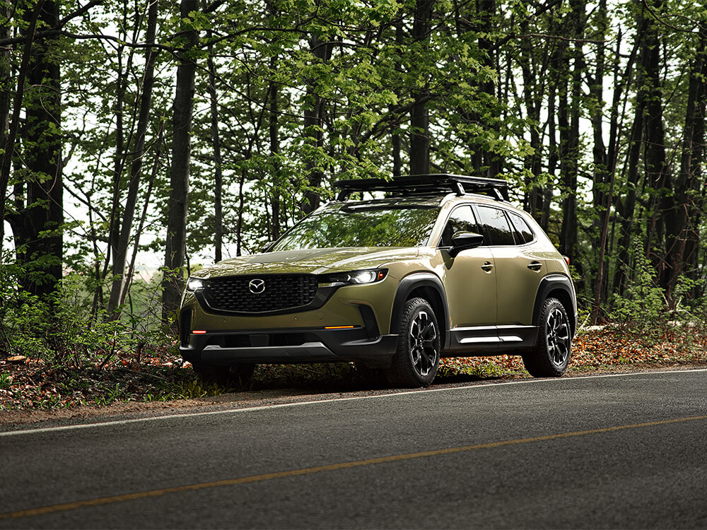 CX-50 in Zircon Sand Metallic parked on side of a paved road amongst trees.