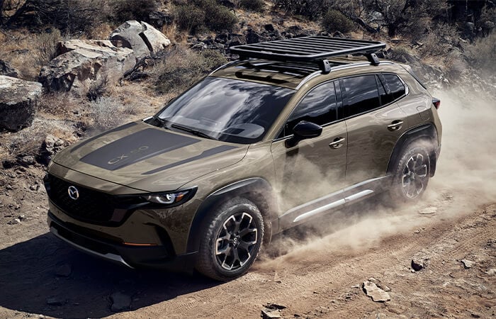 Zircon Sand Metallic CX-50 with roof rack drives up dusty track.