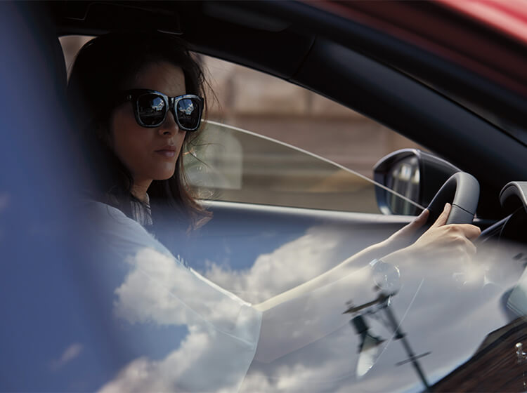 View through passenger’s side window, driver wearing sunglasses inside the Mazda3 sedan grips the wheel.