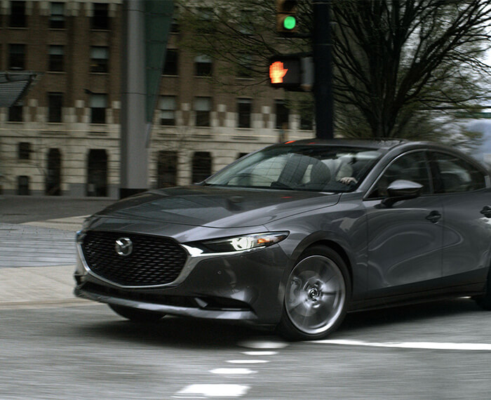 Mazda3 sedan making a tight right turn at a city crosswalk.