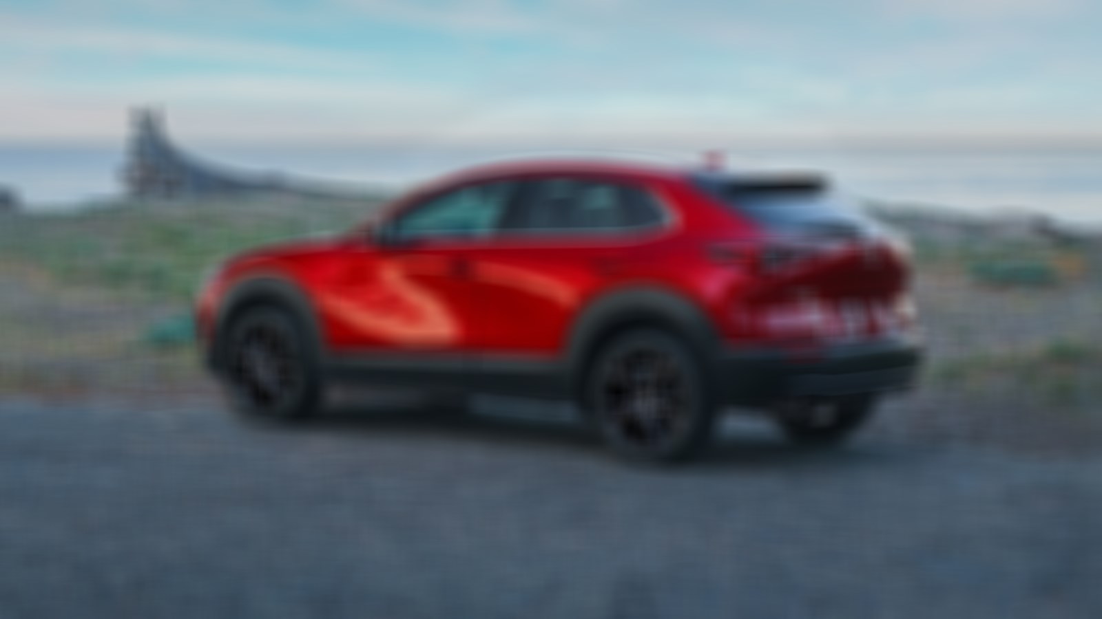 Un VUS multisegment Mazda CX-30 rouge vibrant cristal métallisé garé sur une route de gravier surplombant un vaste lac.