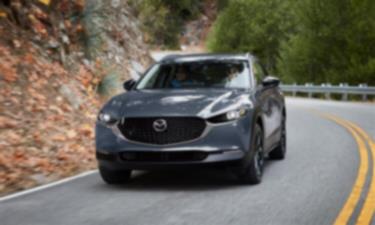 Un Mazda CX-30 gris mécanique métallisé prend un léger virage sur une route escarpée. 