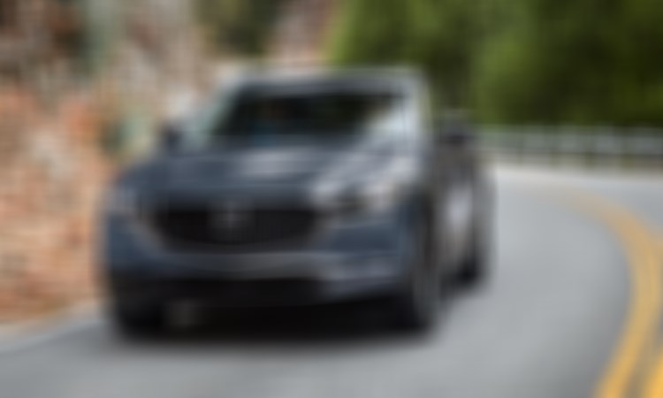 Un Mazda CX-30 gris mécanique métallisé prend un léger virage sur une route escarpée. 