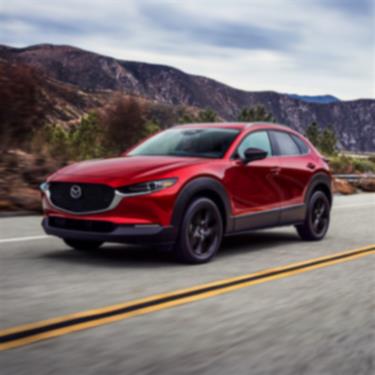 Un Mazda CX-30 rouge vibrant cristal métallisé parcourt une route montagneuse. 