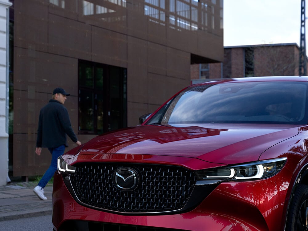Un Mazda CX-5 rouge vibrant cristal métallisé avec la finition Sport Design circule dans une rue. 