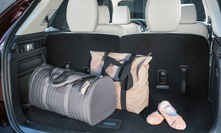 Le hayon d’un CX-90 ouvert révèle un sac de sport gris, un sac à linge beige et des ballerines roses dans l’espace de chargement.  