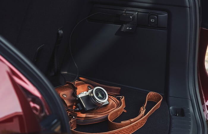 Par le hayon d’un CX-90, on découvre un sac en cuir brun et un appareil photo dans l’espace de chargement.