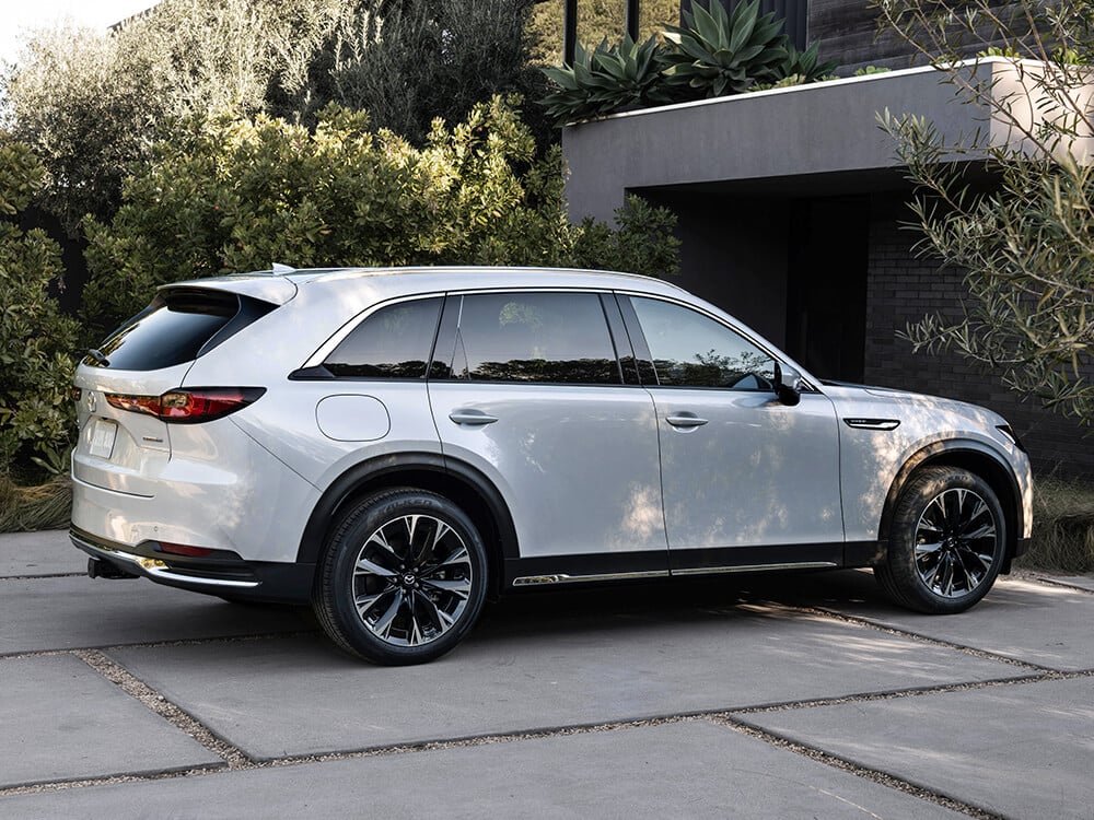 Arctic White CX-90 parked in driveway well shaded by surrounding greenery. 
