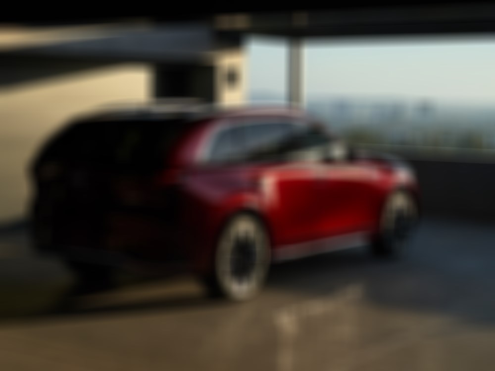 Un CX-90 rouge artisan garé dans un stationnement avec vue sur un paysage urbain au coucher du soleil.