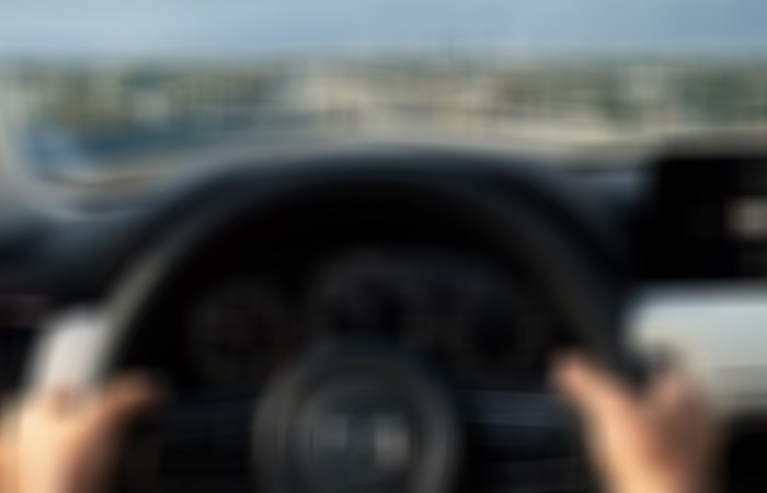 Vue du tableau de bord et des deux mains du conducteur sur le volant pendant que la CX-90 est en mouvement.