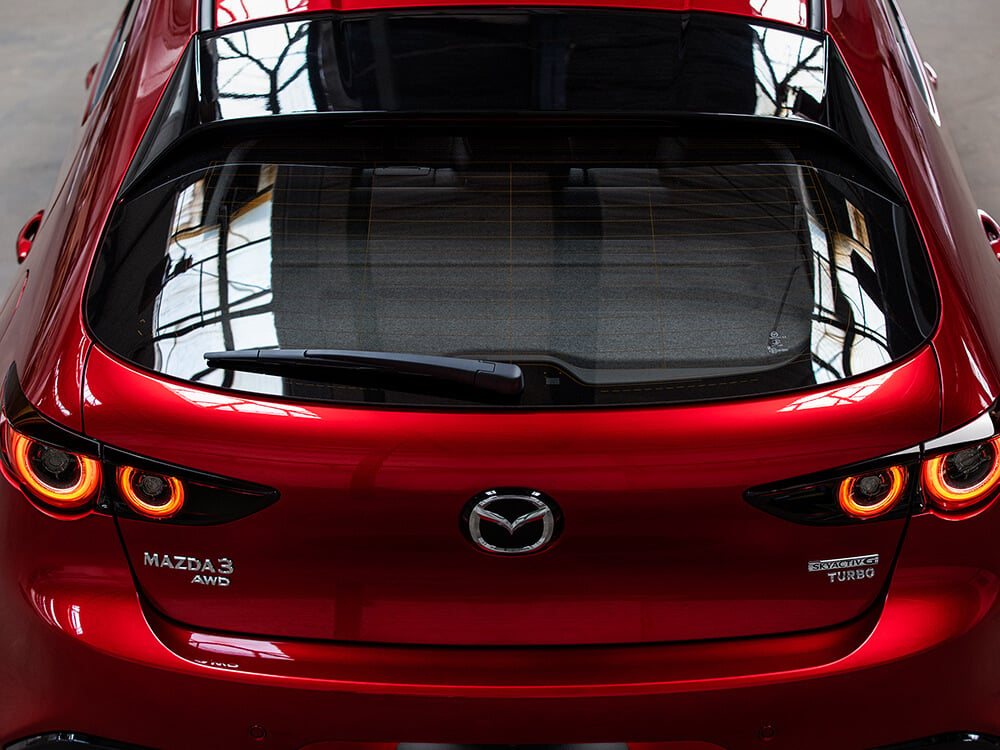 Vue en contre-plongée de l’arrière d’une Mazda3 Sport; on voit l’espace de chargement à travers la vitre du hayon.