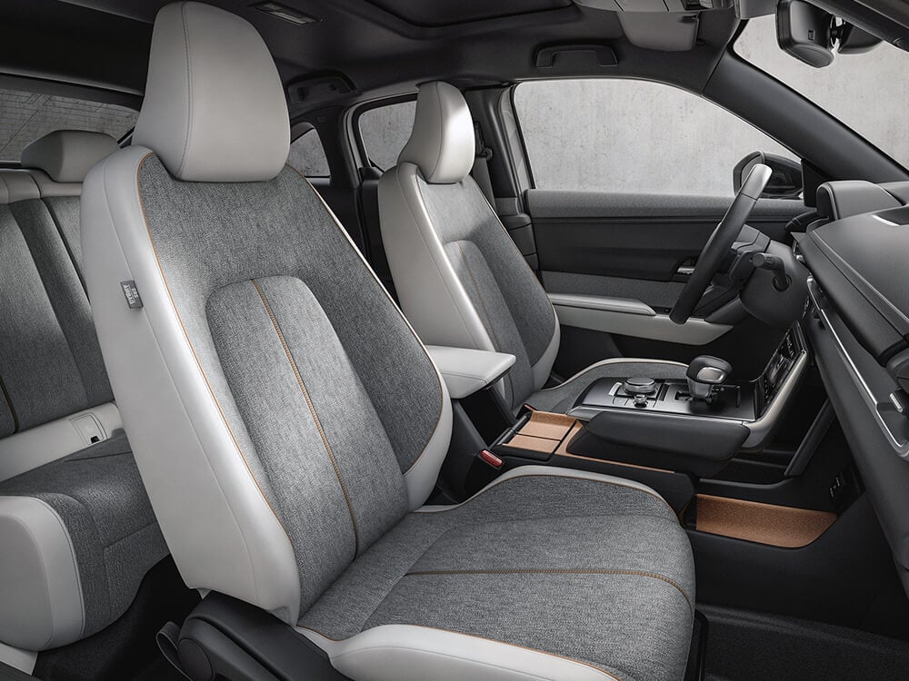 Shot from the passenger’s side inside the MX-30 details the spacious Pure White/Light Grey Leatherette front seating and cork of the centre console.  