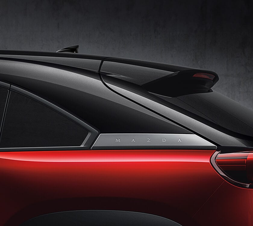 Closeup of “MAZDA” badge behind the rear seat windows of a Soul Red Crystal Metallic Multi-Tone MX-30. 