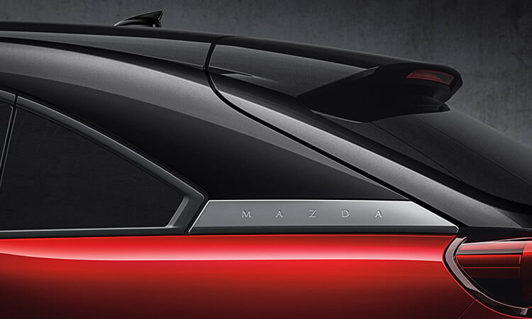 Closeup of “MAZDA” badge behind the rear seat windows of a Soul Red Crystal Metallic Multi-Tone MX-30. 