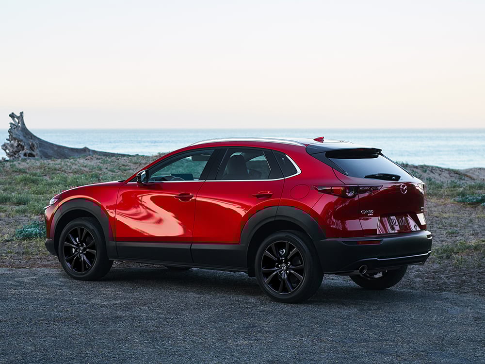 Plan de profil au 7/8 d’un CX-30 rouge vibrant cristal métallisé garé, avec un lac et l’horizon en arrière-plan.