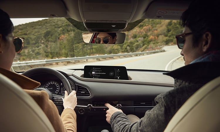 Un CX-30 circulant sur une route de montagne; vue intérieure à partir des sièges arrière vers le conducteur et le passager avant. 