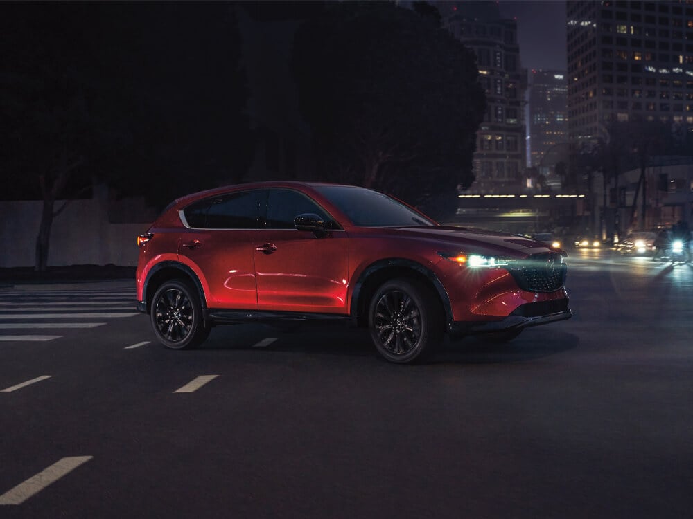 Soul Red Crystal Metallic Mazda CX-5 with Sport Design trim approaches on urban street. 