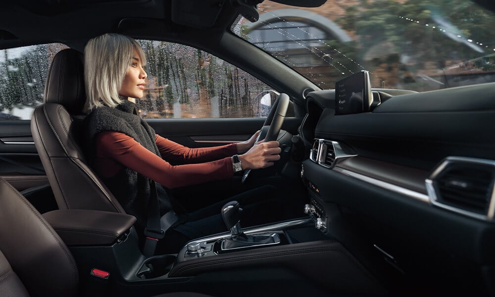 Vue prise du siège passager d’une femme conduisant un CX-5 avec de la pluie visible à travers la fenêtre.