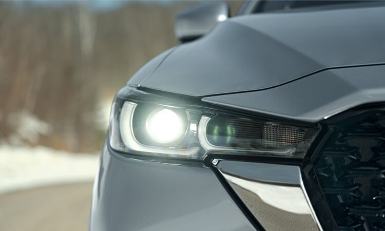 Close up of front right side headlight, hood, front panel and side of grille of Machine Grey Metallic Mazda CX-5.  